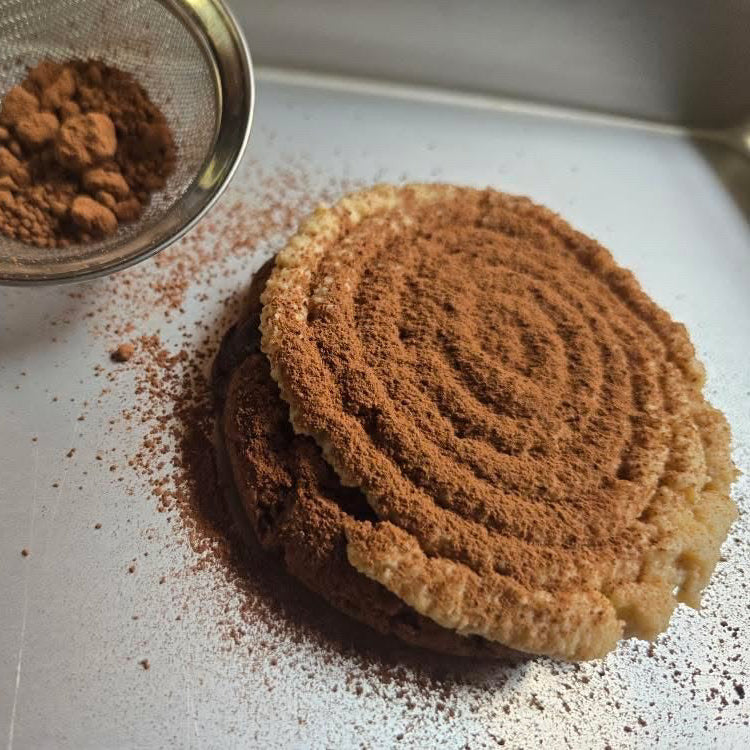 Cinnamon roll with a sifter of cinnamon on a metal surface
