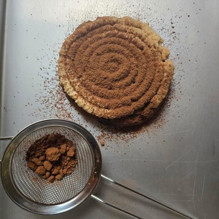 Cinnamon powder in a metal sieve next to a pile of ground cinnamon on a metallic surface
