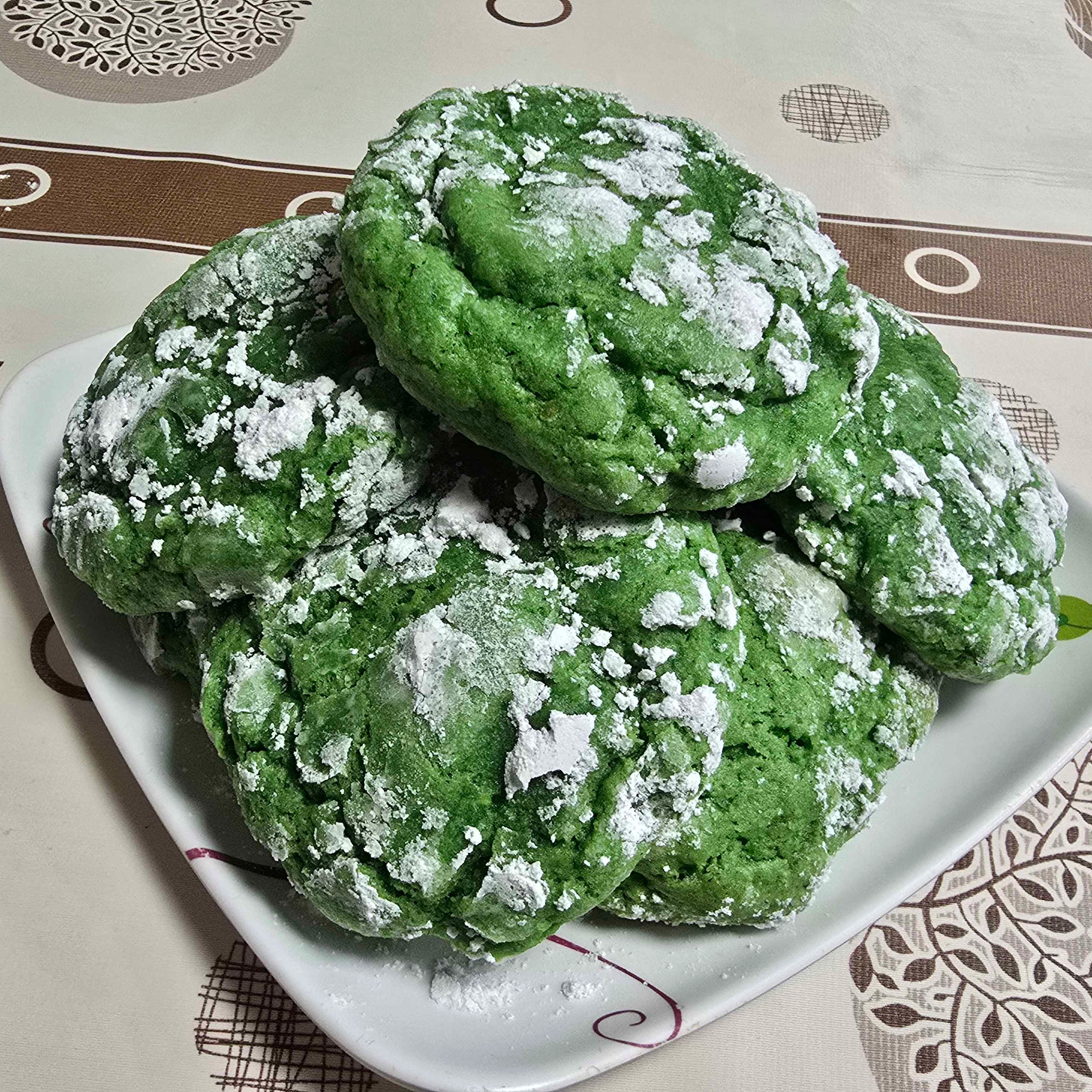 Green cookies with powdered sugar on a white plate on a patterned tablecloth
